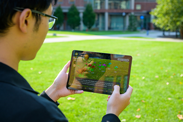 A student holding a tablet displaying information as they walk on green grass.